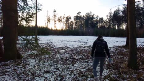 Shot-of-a-woman-wearing-winter-clothes-walking-alone-on-snow-covered-forest-path-at-sunrise