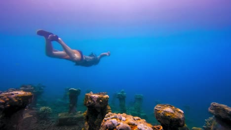 Buceador-Nadando-Sobre-El-Monumento-De-Las-Rocas-En-El-Mar-De-Aguas-Azules,-Bali,-Indonesia