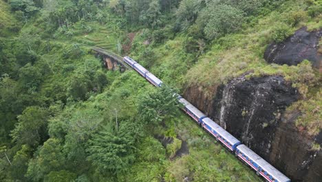 Aerial-view-over-a-train-running-through-a-lush-valley-near-Ella,-Sri-Lanka