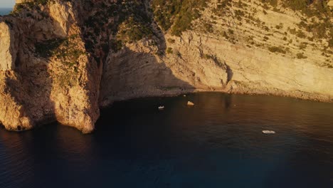 Aerial-shot-starting-big-and-descending-onto-a-group-of-people-partying-in-a-boat-along-the-Ibiza-cliffs