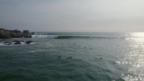 Surfers-surfing-next-to-rocks,-over-Rough-sea-with-waves,-Aerial-static-shot