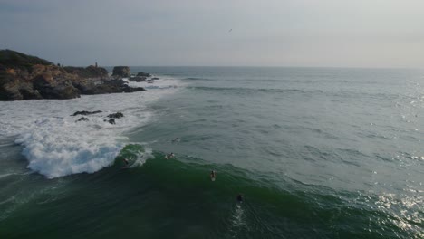 Mar-Agitado-Con-Olas,-Surfistas-Surfeando-Junto-A-Rocas