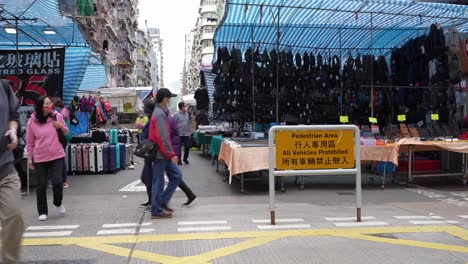 People-walk-by-clothing-market-on-busy-street-in-Mong-Kok,-Hong-Kong