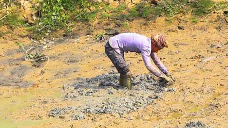 Male-Worker-Standing-In-Knee-Deep-In-Mud-Digging-And-Searching-For-Fish-In-Bangladesh