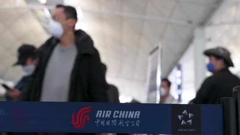 Das-Logo-Der-Chinesischen-Fluggesellschaft-Air-China-Ist-Auf-Einem-Warteschlangenband-Im-Vordergrund-Zu-Sehen,-Während-Sich-Flugpassagiere-An-Einem-Check-in-Schalter-Am-Internationalen-Flughafen-Chek-Lap-Kok-In-Hongkong-Anstellen