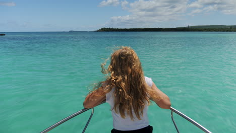 Young-girl-with-thick-hair-riding-the-bow-motorboat-as-it-speeds-towards-the-Isle-of-Pines,-New-Caledonia