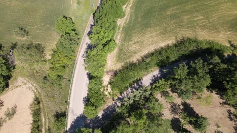 Bird's-eye-view-drone-shot-of-a-car-driving-on-a-remote-road-in-the-countryside-of-Abruzzo-in-Italy-in-4k