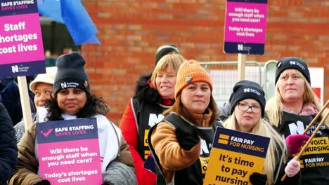 Unterfinanzierte-Und-überarbeitete-NHS-Mitarbeiter-Im-Whiston-Hospital-Protestieren-An-Der-Streikpostenlinie-Mit-Transparenten-Und-Fahnen,-Die-Faire-Lohnbedingungen-Fordern
