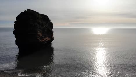 Aerial-Silhouette-View-Of-Lone-Sandstone-Sea-Stack-Alone-Surrounded-By-Calm-Sea-Waves-Off-Ladram-Bay