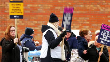 Underfunded-and-overworked-NHS-workers-at-Whiston-hospital-in-Merseyside-protest-on-the-picket-line-with-banners-and-flags-demanding-fair-pay