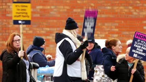 Unterfinanzierte-Und-überarbeitete-NHS-Arbeiter-Im-Whiston-Hospital-In-Merseyside-Protestieren-An-Der-Streikpostenlinie-Mit-Transparenten-Und-Fahnen-Und-Fordern-Eine-Faire-Bezahlung