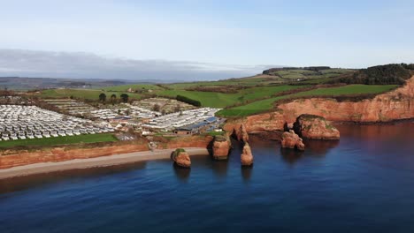 Aerial-View-Of-Ladram-Bay-Holiday-Park-Overlooking-Beach-And-Sandstone-Sea-Stacks-On-Clear-Sunny-Day