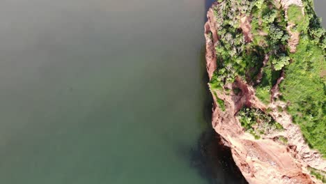 Camera-glides-over-a-grass-covered-cliffside-rock-in-Ladram-Bay,-capturing-the-beauty-of-the-natural-landscape-and-serene-waters-below