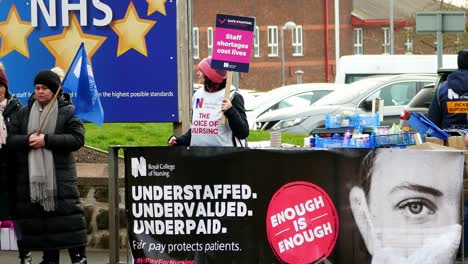 Overworked-NHS-workers-at-Whiston-hospital-in-St-Helens,-Merseyside-strike-on-the-picket-line-with-banners-and-flags-demanding-fair-pay