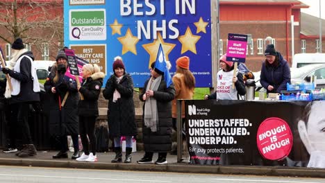Überlastete-NHS-Mitarbeiter-Streiken-Im-Krankenhaus-In-St.-Helens-Und-Protestieren-An-Der-Streikpostenkette-Mit-Transparenten-Und-Fahnen,-Die-Eine-Faire-Bezahlung-Fordern