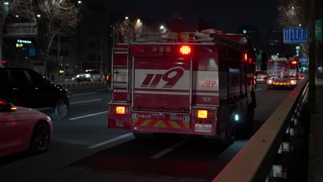 Los-Camiones-De-Bomberos-Con-Luces-Rojas-Intermitentes-De-Emergencia-Se-Detienen-En-El-Bordillo-De-La-Carretera-Por-La-Noche-En-Seúl,-Los-Bomberos-Salen-Rápidamente-De-Los-Camiones-De-Bomberos-Y-Se-Apresuran-Al-Lugar-Del-Accidente