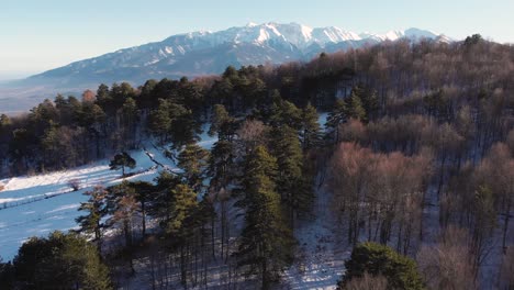 Aerial-Drone-revealing-shot-Mount-Olympus-winter-snow-fly-over-forest-foreground