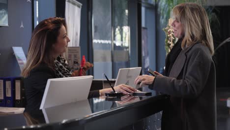 Blond-female-customer-collects-her-car-keys-at-the-dealership-at-the-counter,-the-brunette-saleswoman-smiles-at-her