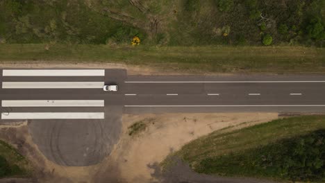 Aerial-top-down-shot-of-car-driving-on-emergency-airstrip-road-in-Uruguay