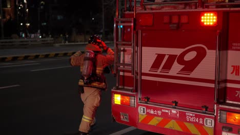 Koreanischer-Feuerwehrmann-In-Einem-Brandschutzanzug,-Der-Nachts-In-Zeitlupe-Mit-Einem-Feuerwehrauto-Auf-Der-Straße-In-Der-Innenstadt-Von-Seoul-Läuft