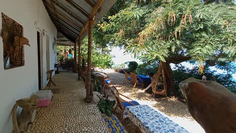 Wunderschönes-Afrikanisches-Haus-Auf-Der-Insel-Bubaque-Mit-Holzstühlen-Unter-Den-Bäumen-Und-Blick-Auf-Das-Meer