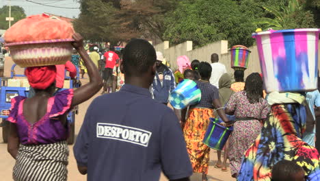 Many-people-circulating,-women-passing-by-with-colorful-buckets-on-their-heads-carrying-fish-and-other-goods-on-the-access-road-to-the-port-of-bandim