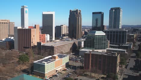 Beautiful-aerial-view-of-downtown-cityscape-of-Birmingham,-Alabama-approaching-skyscrapers-in-front-of-parking-areas-in-bustling-metropolitan-district