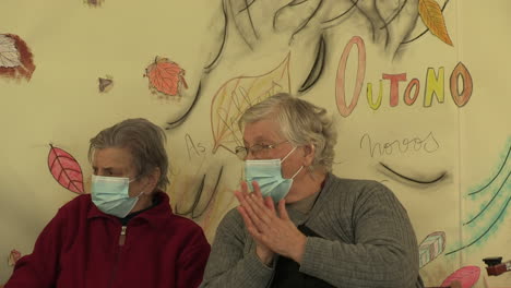 Two-elderly-ladies-are-talking-with-a-COVID-19-masks-their-faces,-the-painted-back-wall-mentioning-the-arrival-of-autumn