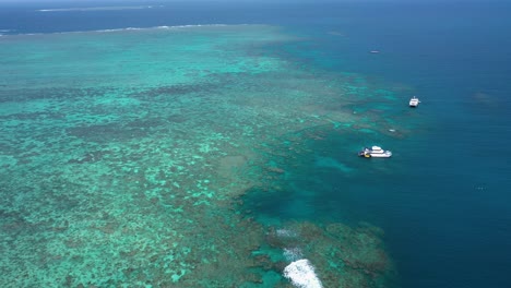 Great-Barrier-Reef-reverse-drone-shot-of-boats-and-coral-ecosystem,-near-Cairns,-Queensland,-Australia