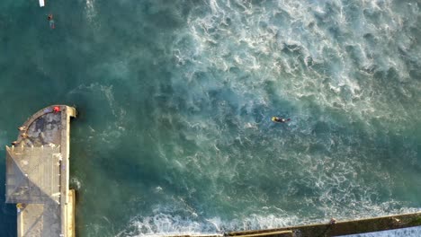 Birdseye-view-of-Surfers-and-Bodyboarders-at-the-end-of-the-pier-on-Waikiki-Walls,-Hawaii