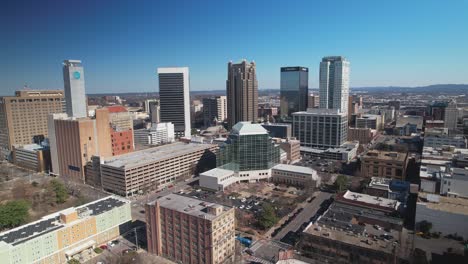 Beautiful-aerial-view-of-downtown-cityscape-of-Birmingham,-Alabama-approaching-skyscrapers-in-front-of-a-blue-skyline
