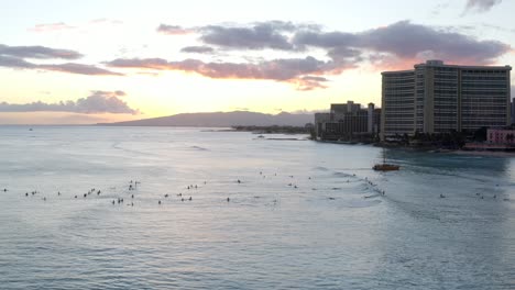 Vista-Aérea-De-Extracción-Mientras-Multitudes-De-Surfistas-Disfrutan-De-La-Puesta-De-Sol-Sobre-La-Playa-De-Waikiki-En-Hawaii
