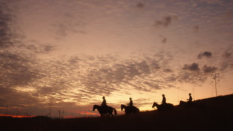 4-Cowboys-Im-Frühen-Morgenlicht,-Während-Sie-Einen-Malerischen-Hügel-Hinunterreiten