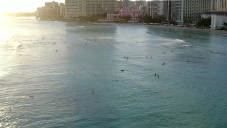 Lujosos-Condominios-En-La-Playa-De-Waikiki-Al-Atardecer-Orbital-Alrededor-De-Los-Surfistas