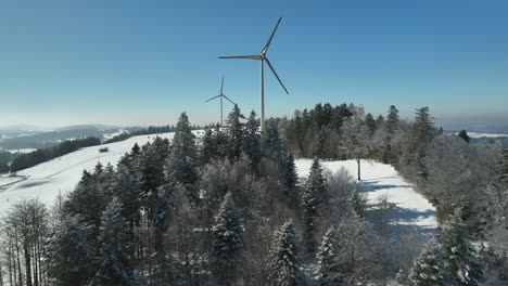 Two-giant-modern-windmills-rotating-in-the-wind-on-top-Jura-mountain-in-Switzerland-on-a-sunny-winter-day