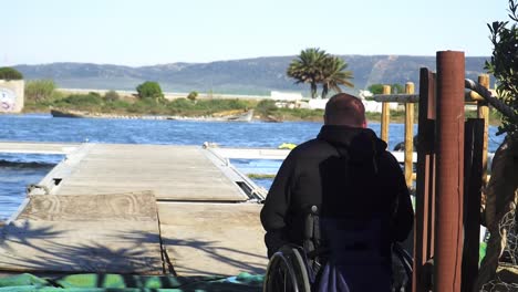 Close-up-of-a-disabled-man-in-a-wheelchair-on-his-back-on-the-dock-of-a-reservoir-ready-for-canoeing