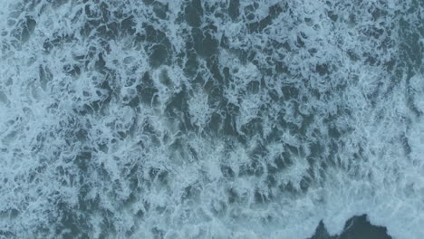An-overhead-drone-shot-captures-the-textures-of-water-as-sea-waves-crush,-foam,-bubble,-and-swirl