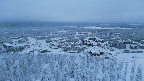 Flying-down-into-the-winter-spruce-forest,-in-the-background-a-panorama-of-the-city-of-Levi