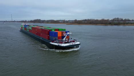 Aerial-View-Along-Starboard-Side-Of-Moonlight-Inland-Motor-Freighter-Sailing-Along-Beneden-Merwede-Carrying-Intermodal-Containers-On-Overcast-Day