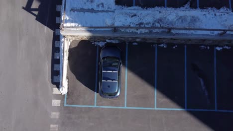 Aerial-top-up-view-of-blue-car-parked-in-snowy-outdoor-car-park