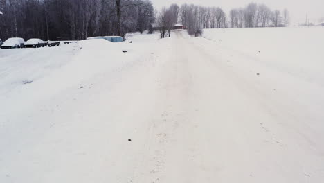 Empty-snow-covered-slippery-road-on-overcast-winter-day,-low-aerial-dolly-in
