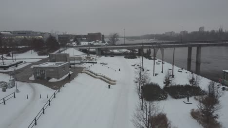 Drohnenvideo-Eines-Verschneiten-Flussufers-In-Warschau,-Polen,-Mit-Blick-Auf-Eine-Brücke-Und-Autos-Mit-Verkehr