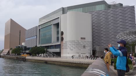 Kunstmuseum-Von-Hongkong-In-Tsim-Sha-Tsui,-Das-Moderne-Gebäude-Und-Eine-Chinesische-Person-Mit-Einer-Maske,-Die-Fotos-Macht
