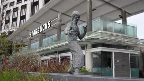 Estatua-De-Bruce-Lee-En-La-Avenida-De-Las-Estrellas-En-Hong-Kong,-Starbucks-Cafe-En-El-Fondo