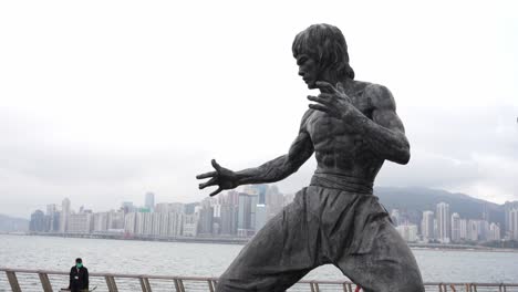 8-De-Febrero---Estatua-De-Bruce-Lee-En-El-Paseo-Estelar-De-Hong-Kong-En-Tsim-Sha-Tsui-Con-El-Horizonte-De-Hong-Kong-En-Segundo-Plano-En-Un-Día-Nublado