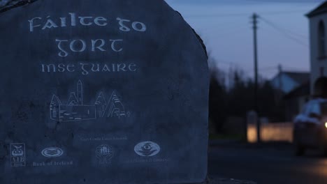 Gort-stone-sign-at-the-entrance-of-town-at-night-and-cars-passing-with-lights-on-in-the-background