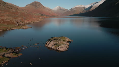 Flying-down-to-hiker-on-island-in-dark-lake-with-snowy-mountain-range-reveal-at-Wasdale-Lake-District-UK