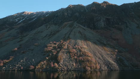 Annäherung-An-Den-Berghang-Entlang-Der-Seeoberfläche-Mit-Sonnenuntergangsstrahlen,-Die-Felsen-Im-Wastwater-Lake-District-Im-Vereinigten-Königreich-Grasen