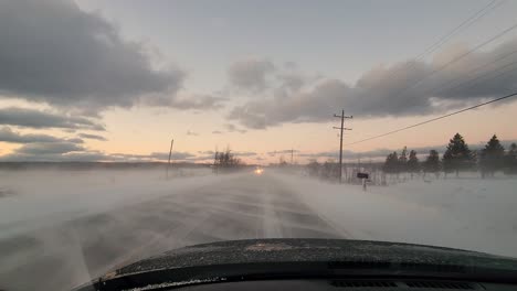 Driving-through-snowy-road-during-Sunset,-snow-covers-the-ground