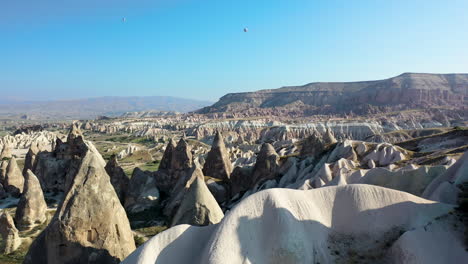 Epic-cinematic-revealing-drone-shot-of-a-lone-man-standing-among-the-fairy-chimneys-and-looking-at-the-mountains-in-Cappadocia,-Turkey